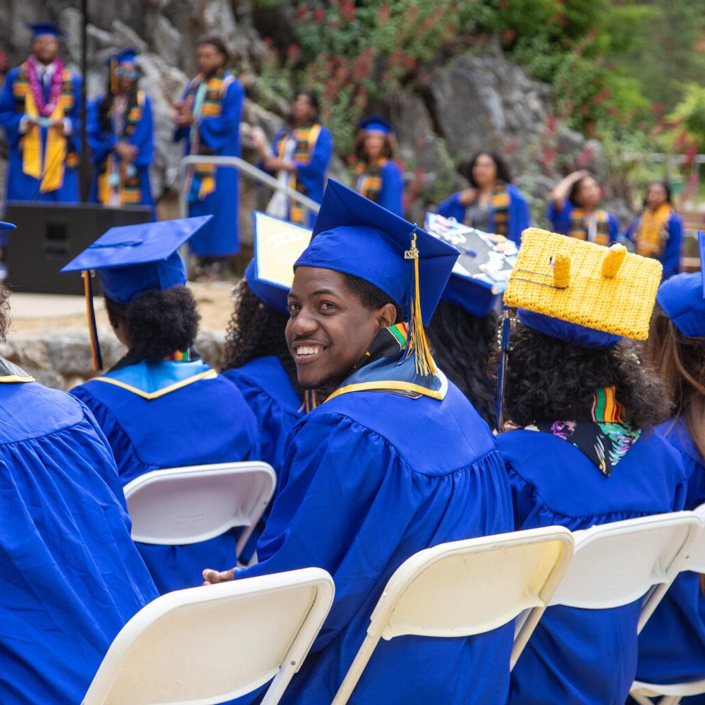 Student seated a tcommencement ceremony smiling and looking at the camera. 